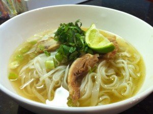A bowl of phở gà with shredded chicken, rice noodles, scallions, herbs, and a lime wedge.
