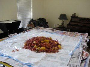 A pile of boiled crawfish, corn, and potatoes poured onto a plastic-covered table at home.
